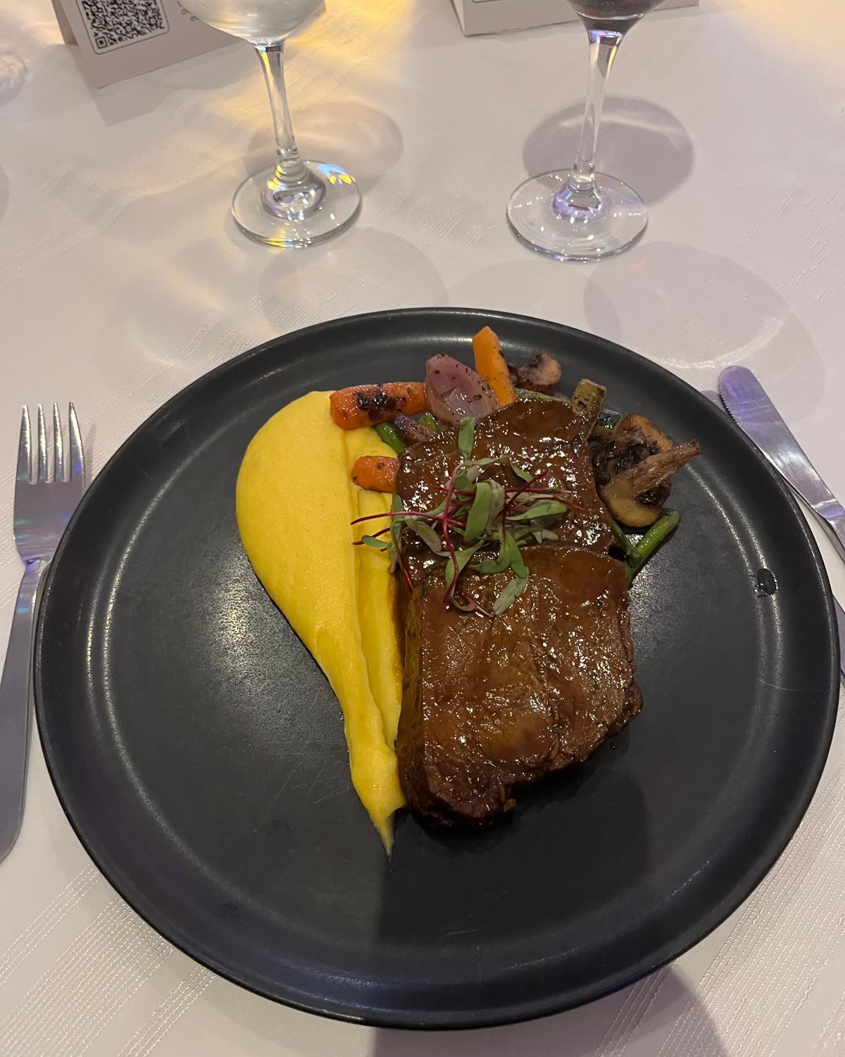 Plato de carne en salsa con puré amarillo y vegetales, servido en la mesa de Joyas Colombianas